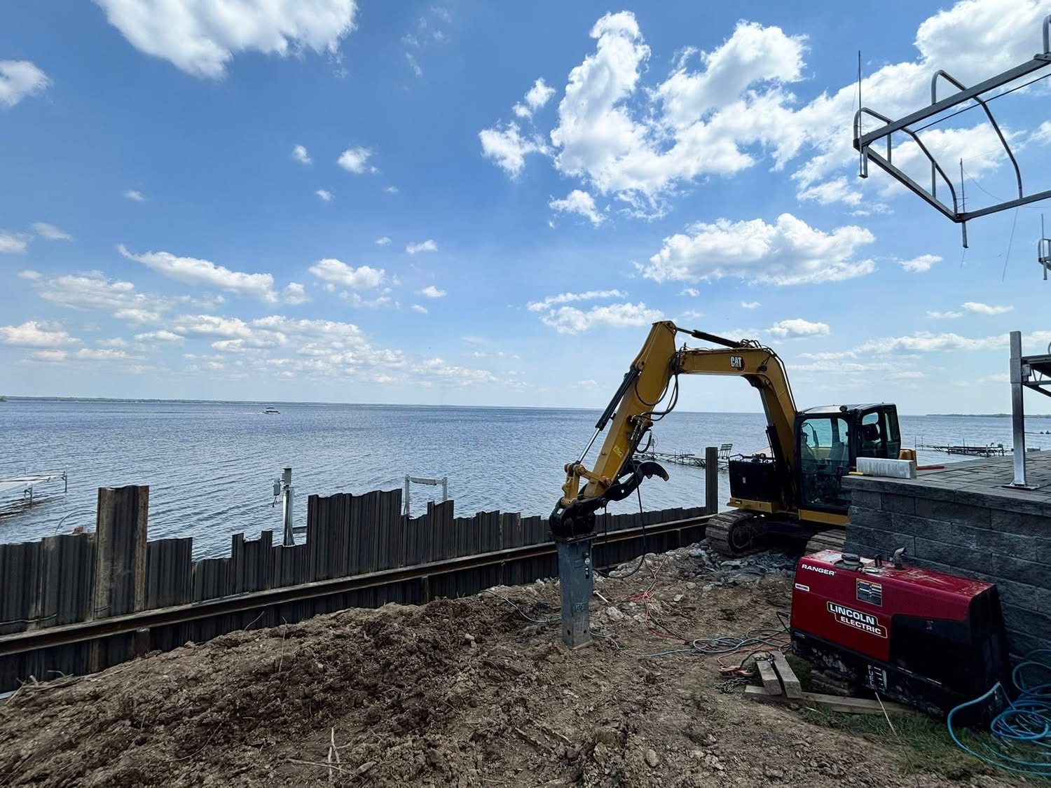 Excavator driving piling for a lakefront seawall and dock foundation