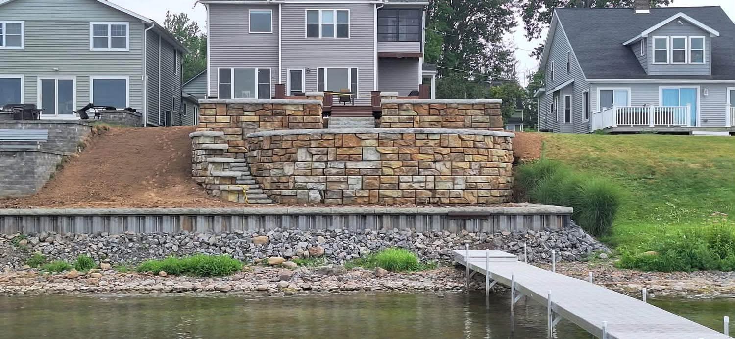 Tiered stone block retaining wall above a steel seawall on a lakefront lot