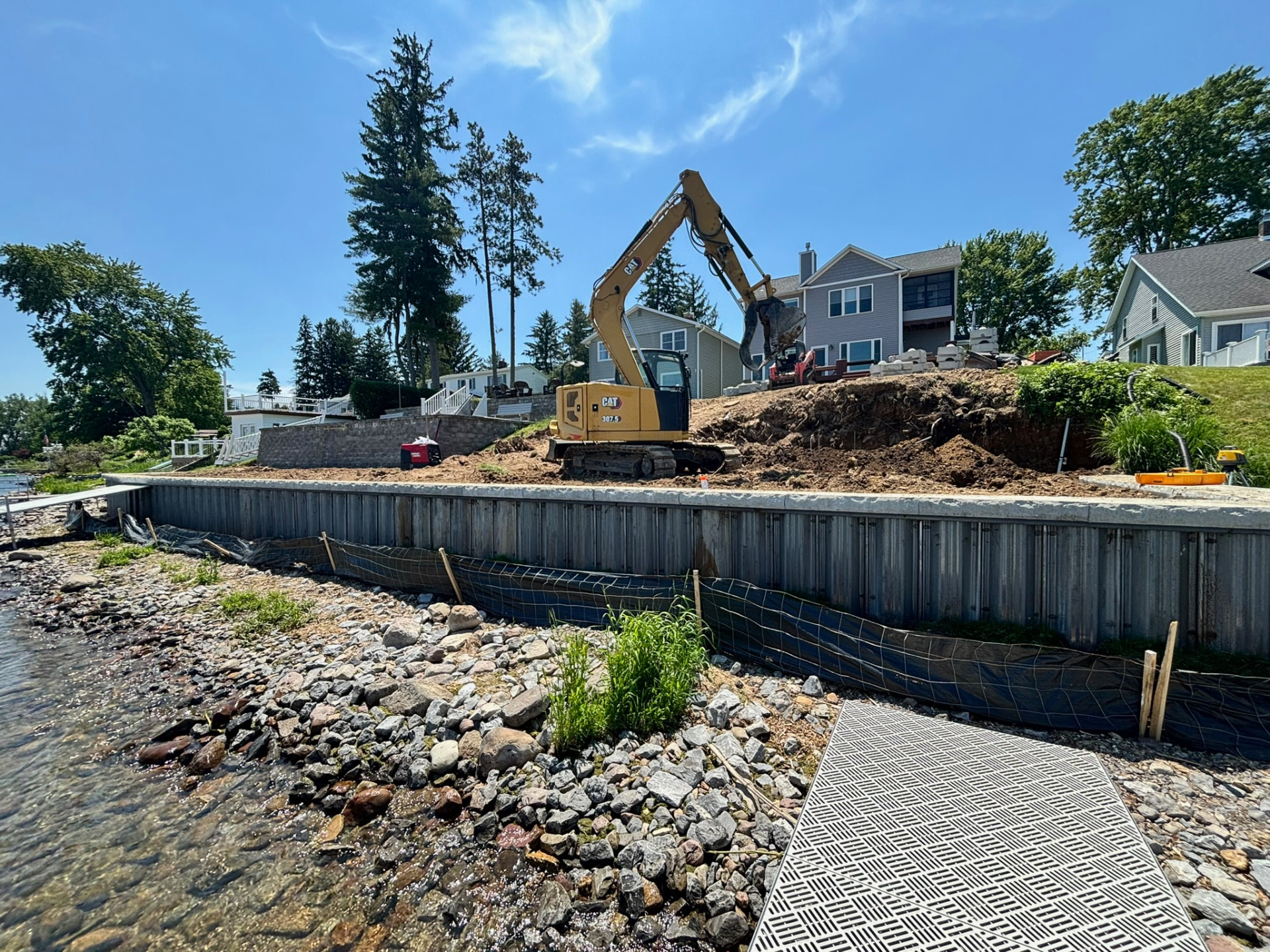 Excavator regrading a lakefront lot behind a newly installed steel sheet pile seawall